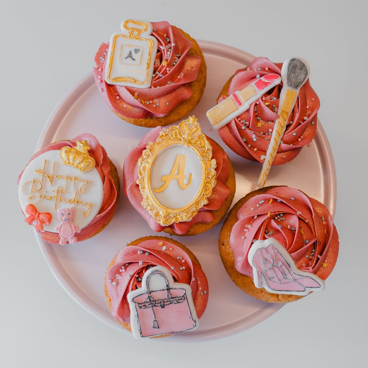 Šest ručno ukrašenih cupcakesa s parfemom, šminkom, torbicom i slovom u zlatnom okviru